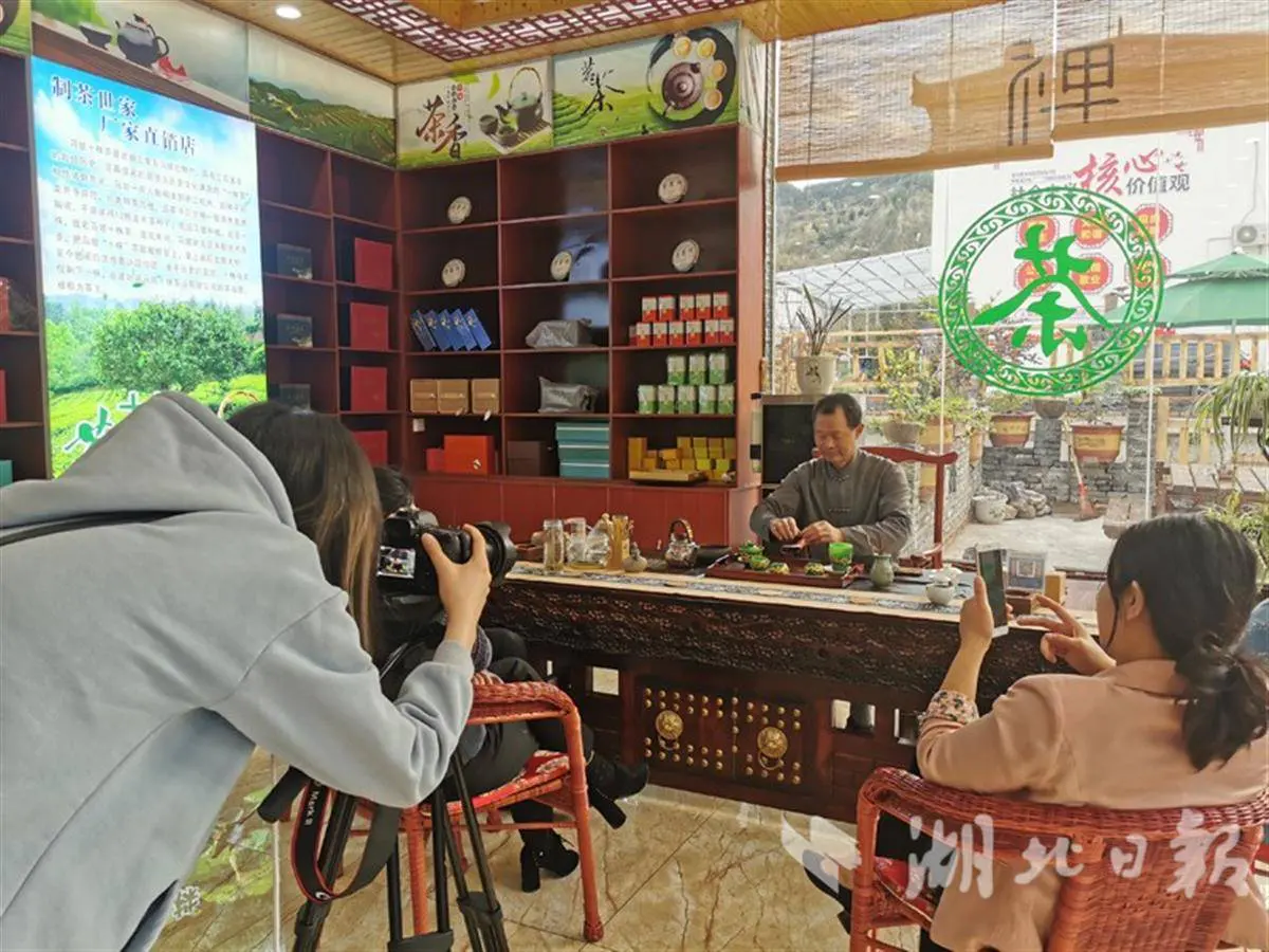 A tea maker filmed by a camera crew and a smartphone in a tea shop