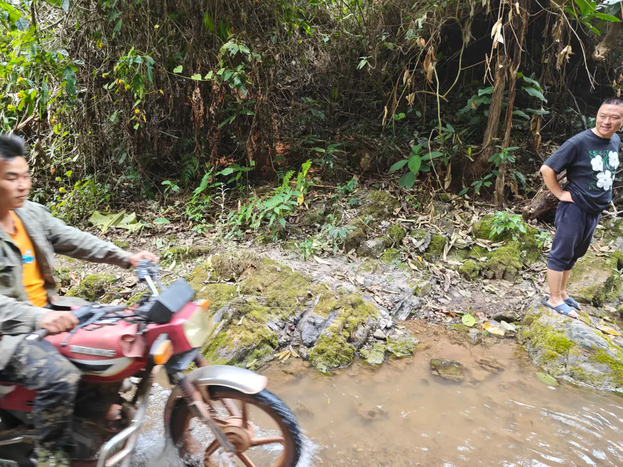 A local rider steering a motorbike through a shallow rocky stream while carrying a woven tea basket